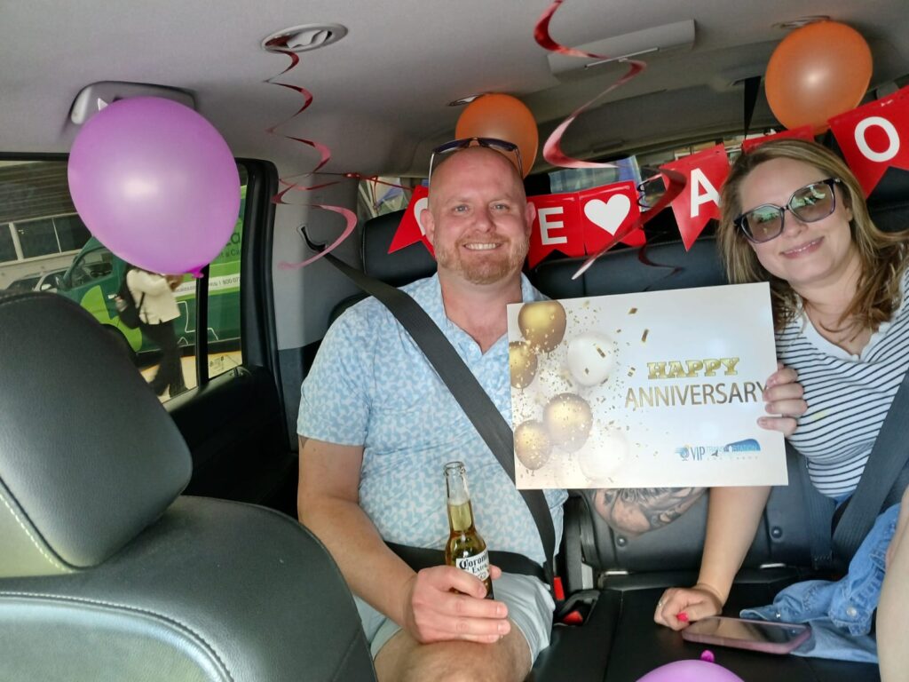  Couple sitting inside a VIP Transportation Los Cabos vehicle decorated with balloons, a TE AMO banner and a Happy Anniversary sign for an SJD airport pickup.